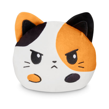 A Plushiverse Cuddly Calico Cat 4” Reversible Plushie designed to look like a cartoonish calico cat with a grumpy expression, created by TeeTurtle.