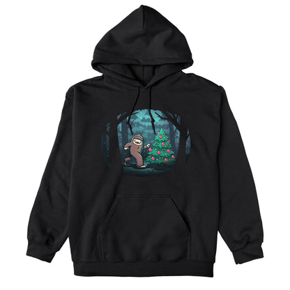 Pullover Hoodie_TeeTurtle black Bigfoot Christmas apparel featuring a sasquatch caught putting holiday decor on a tree in the middle of a snowy forest.