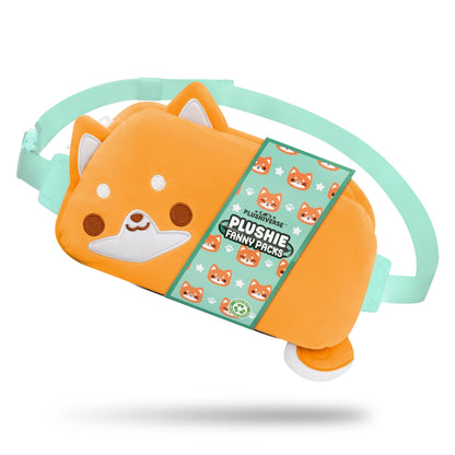 The TeeTurtle Plushiverse Super Shiba Plushie Fanny Pack features a green adjustable strap and offers hands-free functionality. It's packaged with a label adorned with charming small fox graphics and branding, making it a delightful accessory for both style and convenience.