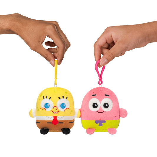 Two hands are holding Plushiverse SpongeBob SquarePants and Patrick Star Plushmates Besties resembling SpongeBob SquarePants (left) and Patrick Star (right). These adorable bag charms by Nickelodeon are perfect for adding a touch of fun to your accessories.