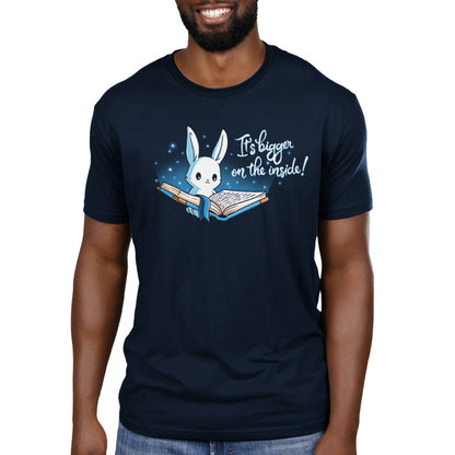 Premium Cotton T-shirt_Teeturtle Books are Bigger on the Inside Navy Blue t-shirt featuring a white rabbit reading a book from which light and sparkles are coming out with a blue ribbon bookmark marking the page with the text "It's bigger on the inside!" written next to it.