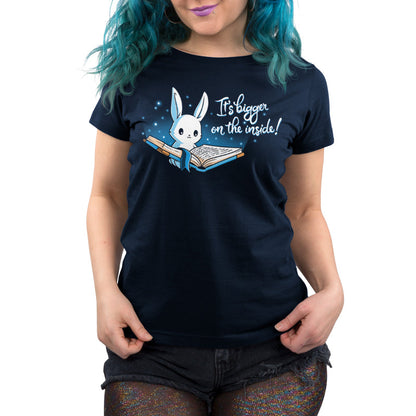 Premium Cotton T-shirt_Teeturtle Books are Bigger on the Inside Navy Blue t-shirt featuring a white rabbit reading a book from which light and sparkles are coming out with a blue ribbon bookmark marking the page with the text "It's bigger on the inside!" written next to it.