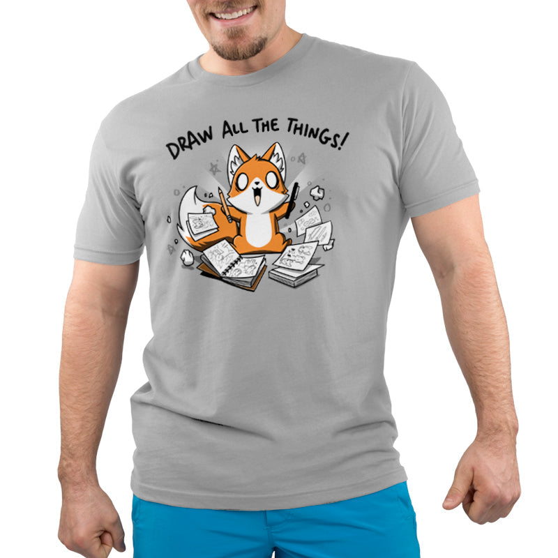 Premium Cotton T-shirt_A cartoon fox enthusiastically holding drawing tools, surrounded by sketchbooks with various drawings. Text above reads "Draw All The Things!" This monsterdigital original Draw all the Things! is crafted from super soft ringspun cotton for ultimate comfort.