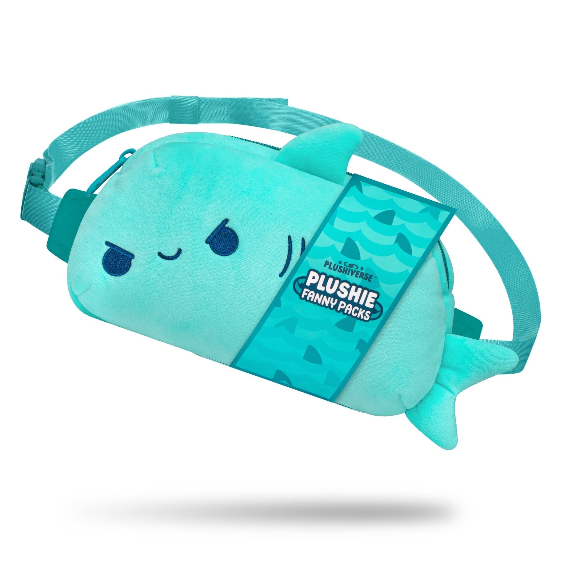 A blue, Plushiverse Jaw-some Shark Plushie Fanny Pack by TeeTurtle shaped like a fish, with a winking face and fin details, against a white background. Featuring an adjustable belt for hands-free functionality, the tag reads "Plushie Fanny Packs.