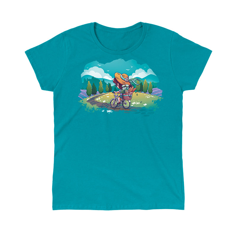 Classic Cotton T-shirt_TeeTurtle Countryside Biking tropical blue t-shirt featuring an illustration of a girl biking on a path in the countryside with bread and flowers in her basket. The path winds through rolling hills and fields of grass with small, white flowers. Green trees line the sides of the path, and lavender bushes are behind the trees, set against a light teal/turquoise sky, with fluffy white clouds and some birds.