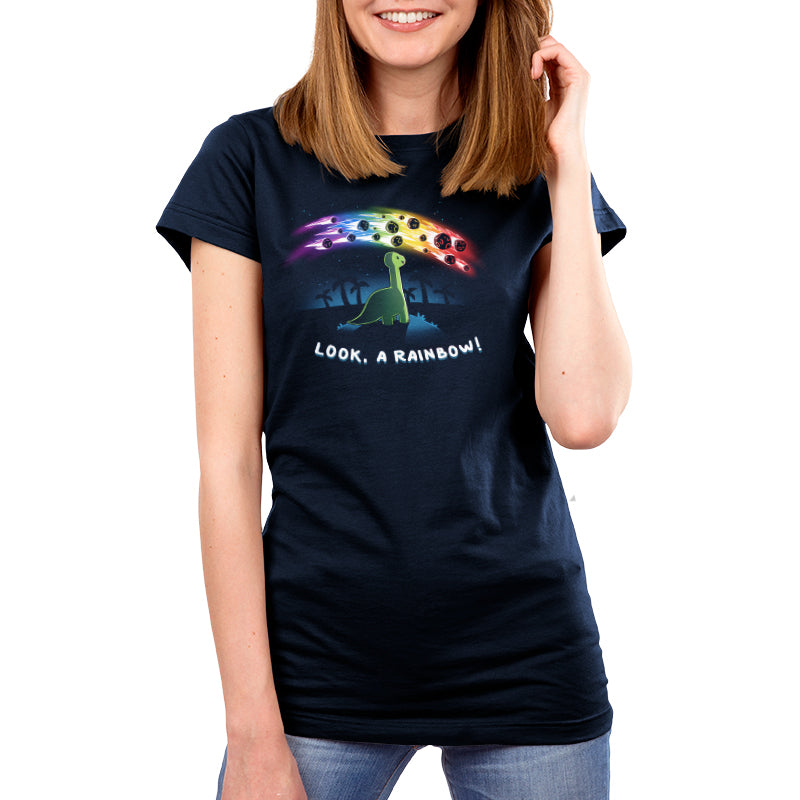 Premium Cotton T-shirt_TeeTurtle Look, a Rainbow! navy blue t-shirt featuring a green dinosaur looking up at rainbow asteroids in the starry night sky. The background is filled with black palm trees in the distance being illuminated from the asteroids, with "LOOK, A RAINBOW!" written underneath the illustration.