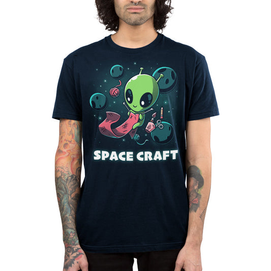 Premium Cotton T-shirt_TeeTurtle Space Craft navy blue t-shirt featuring an illustration of a green alien knitting a red scarf in space surrounded by planets, stars, balls of yarn, and a cup holding scissors, a paint brush and floating pencil. The words 