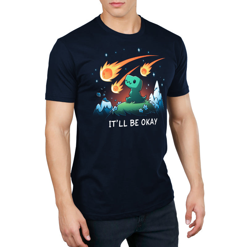 Premium Cotton T-shirt_TeeTurtle It'll Be Okay navy blue t-shirt featuring a green dinosaur who sits on a grassy hill with comet-like objects falling from the sky around them with the words "IT'LL BE OKAY" below them. 