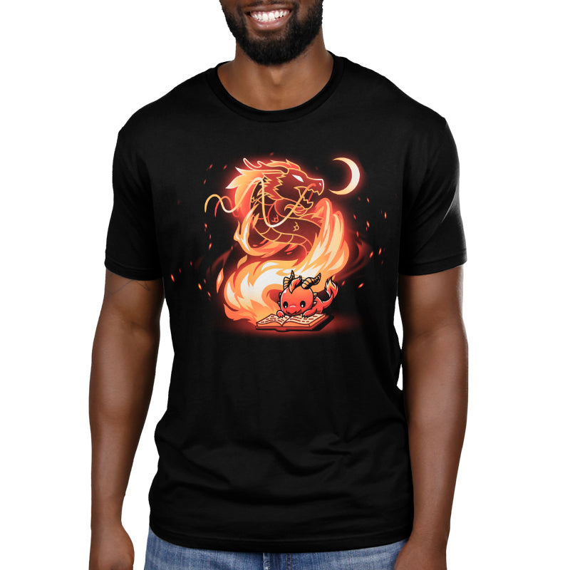 Premium Cotton T-shirt_TeeTurtle Tale Of Scales black t-shirt featuring an illustration of a little red dragon reading a book that has a large, fiery dragon swirling in flames coming out from the book and a small crescent moon in the top right corner near the large dragon's head.