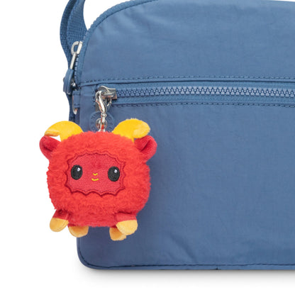 A Lunar New Year Ram Plushie Charm Keychain from TeeTurtle is attached to the side of a blue bag.