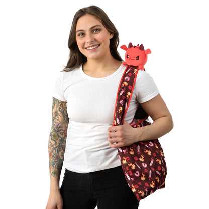 A woman with tattoos holding a TeeTurtle Tabletop Dragon Plushie Tote Bag.