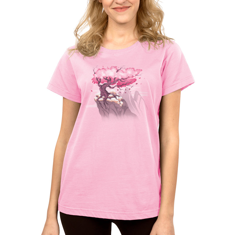 Premium Cotton T-shirt_TeeTurtle Sakura Tree pink t-shirt featuring an illustration of a pink cherry blossom tree on a rocky cliff with mountains in the background. Blossoms and petals are being blown in the wind. 