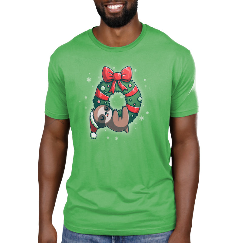 Premium Cotton T-shirt_TeeTurtle We Wish You a Lazy Christmas apple green t-shirt featuring a cartoon sloth in a Santa hat, snoozing while hanging from a festive wreath adorned with red ribbons and ornaments. 