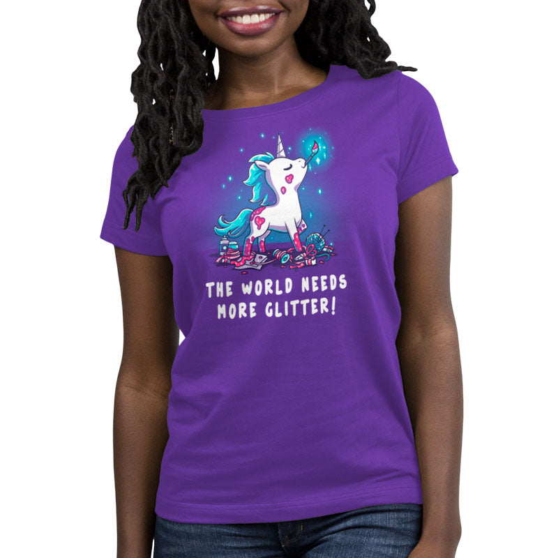 Premium Cotton T-shirt_TeeTurtle The World Needs More Glitter Purple t-shirt featuring a white unicorn holing a paint brush in it's mouth with a blue mane and tail, standing proudly above an assortment of craft supplies. It's covered with patches of pink glitter, one of which is shaped like a heart. Beneath it are the words "THE WORLD NEEDS MORE GLITTER!"