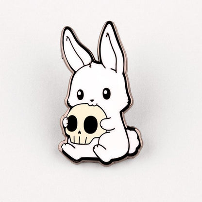 An Adorable Monstrosity Pin with a rabbit holding a skull made of metal by TeeTurtle.