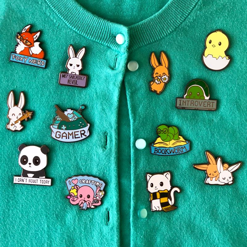 A green cardigan adorned with a collection of Me? Sarcastic? Never. Pins by TeeTurtle, accompanied by care instructions.