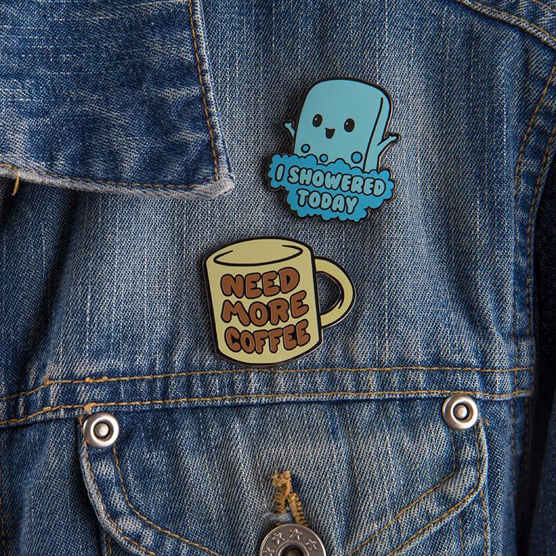 A denim jacket with two TeeTurtle Need More Coffee Pins on it.