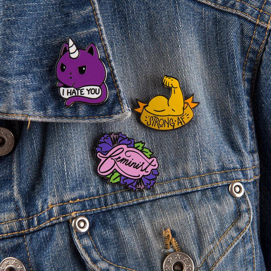 A pair of TeeTurtle denim jackets with three clean Feminist Pin badges on them.